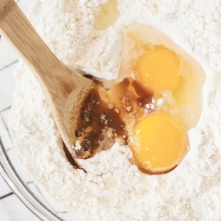 Stock photo of baking bowl containing flour and eggs, being stirred with a wooden spoon.