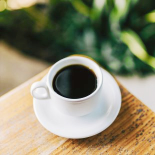 Stock photo of black coffee in a white cup and saucer resting on a wooden table.